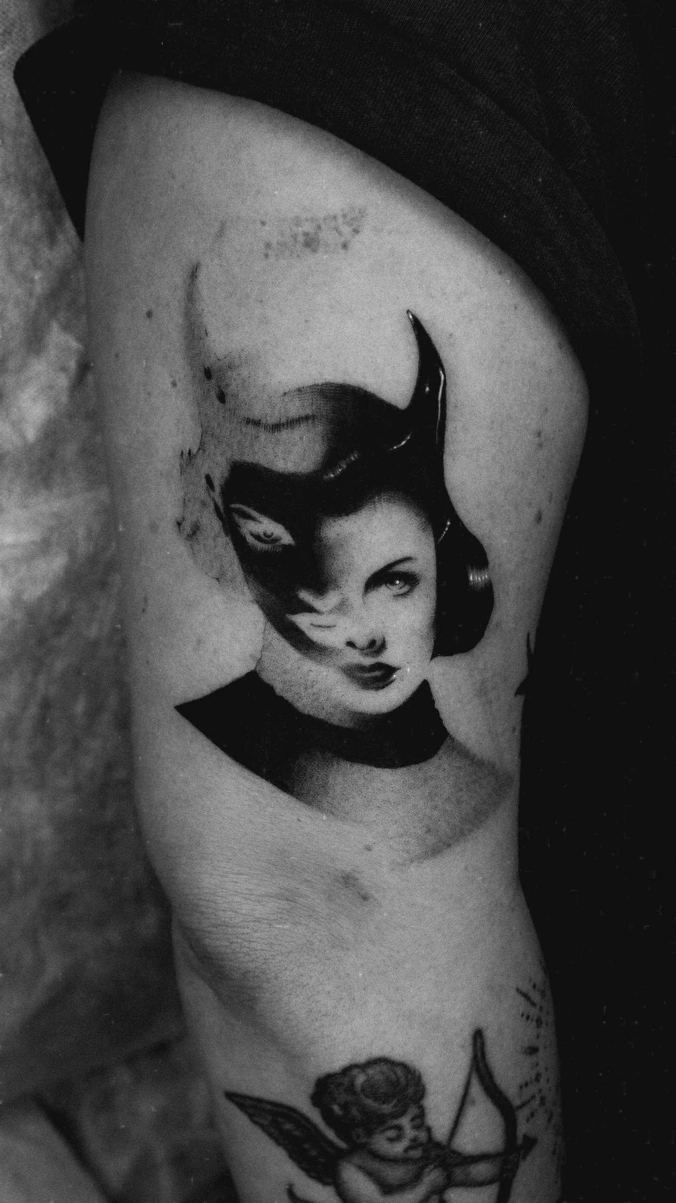 Black and grey upper-arm tattoo of a woman's face in a pointed mask.