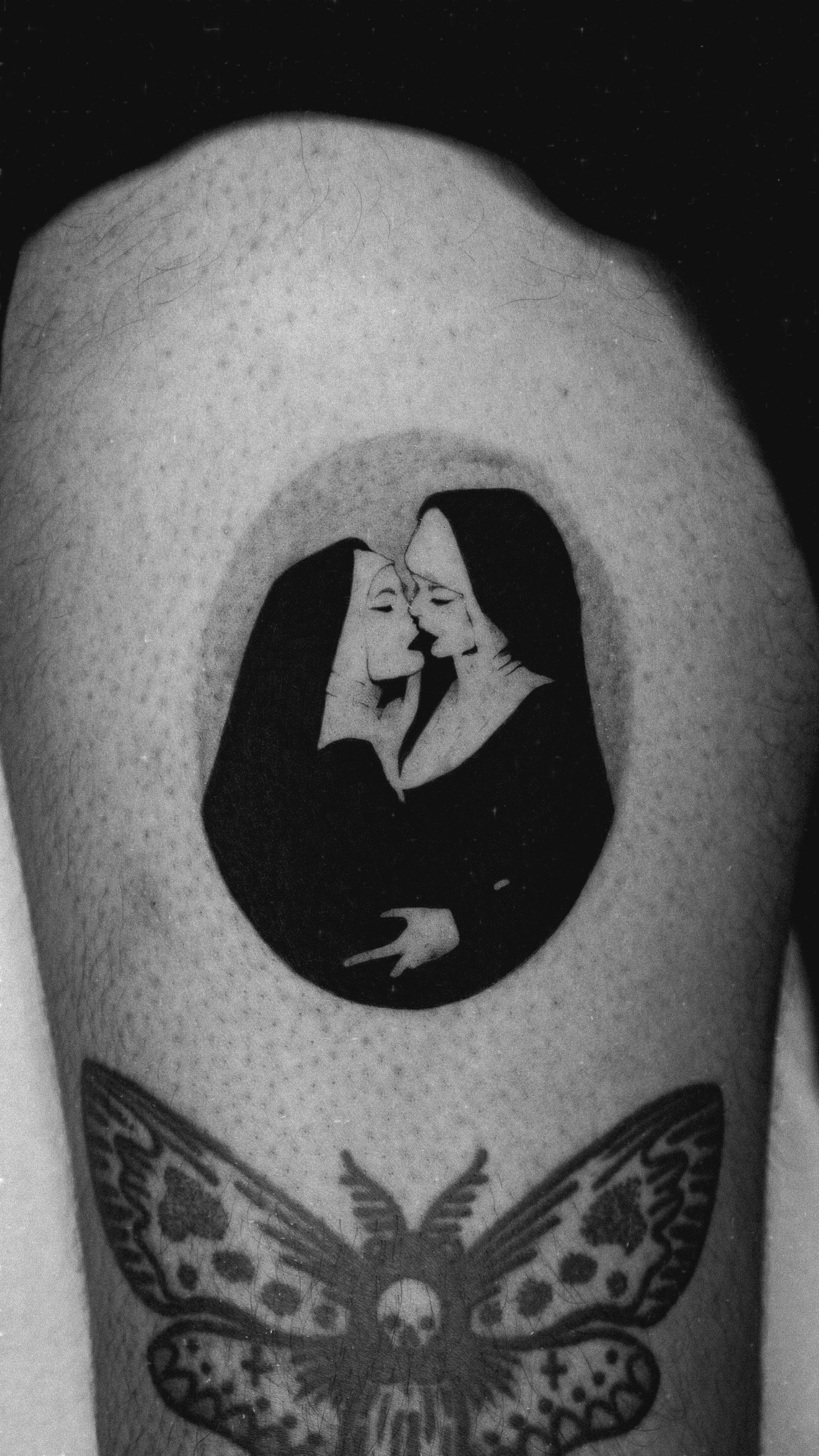 Upper-arm tattoo of a woman in dark clothing with a raised finger, above a moth.