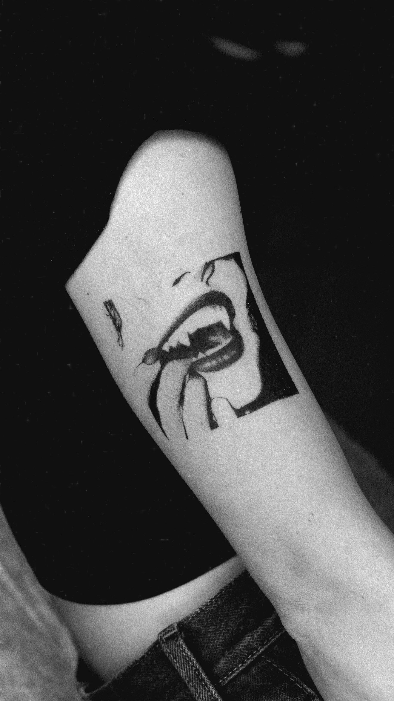 Black and grey upper-arm tattoo of a mouth within an angular frame.