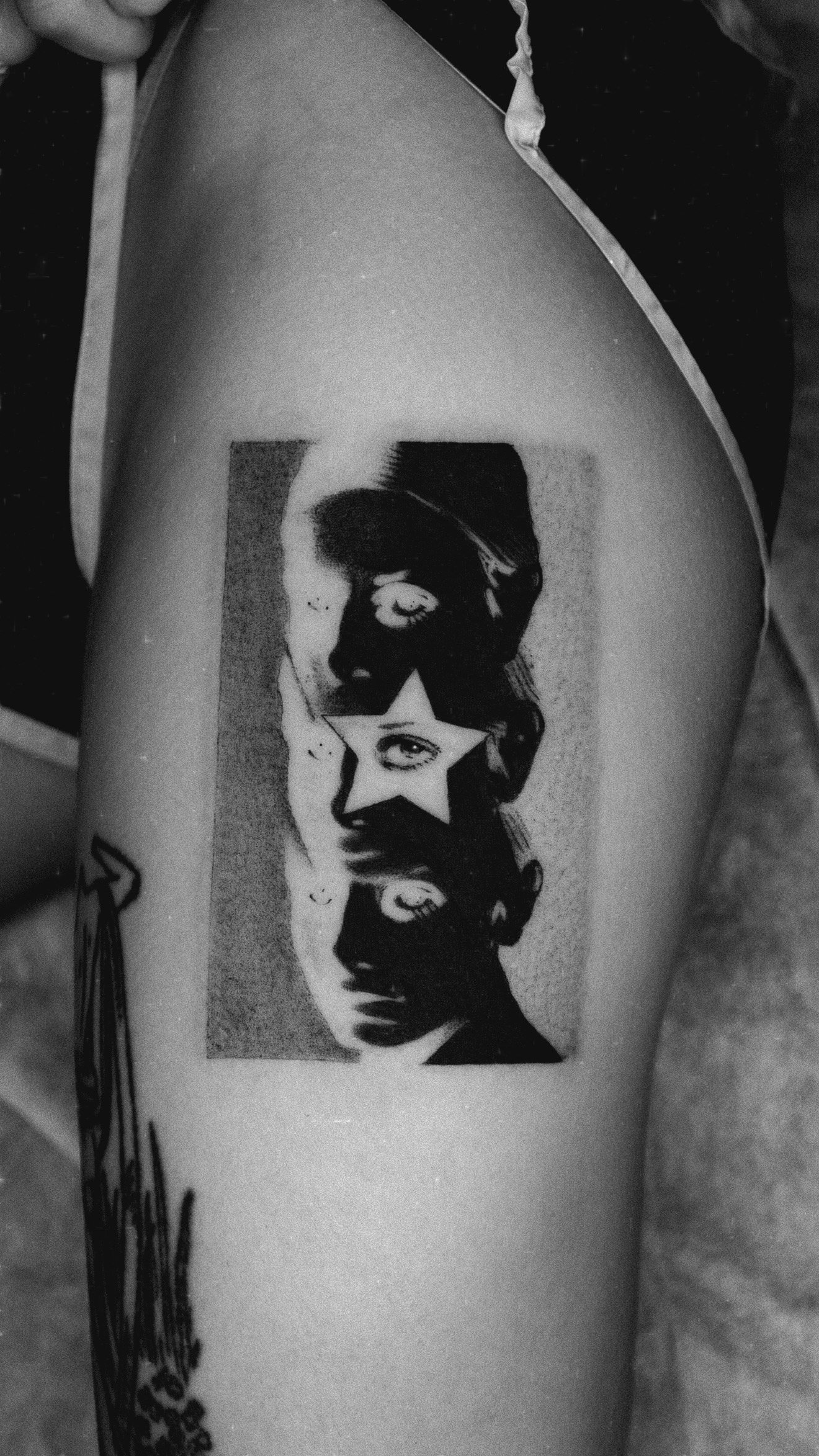 Black and grey upper-arm tattoo with overlapping faces and a star across the central eye.