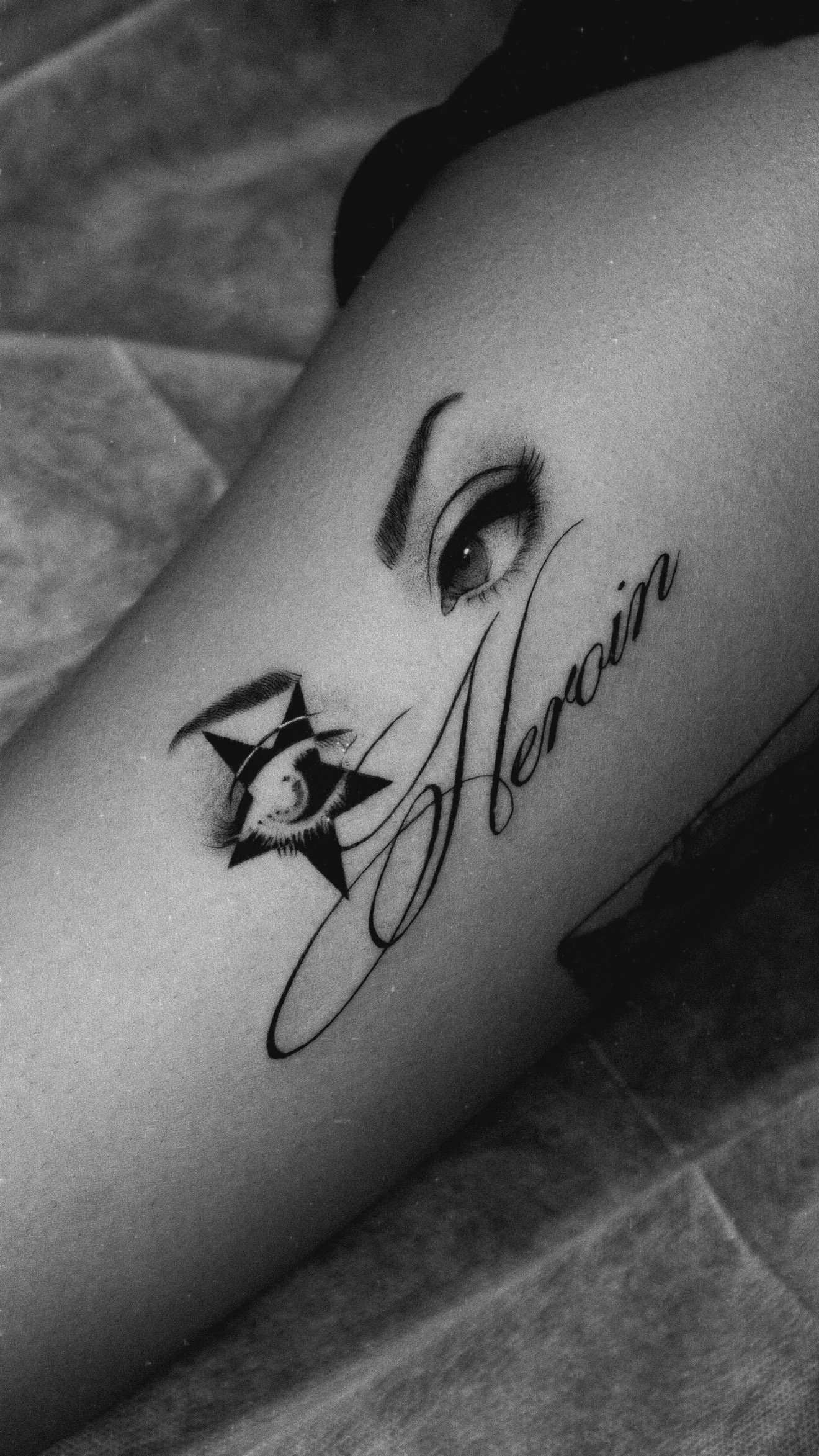 Black and grey tattoo of an eye and star beside the script Heaven.