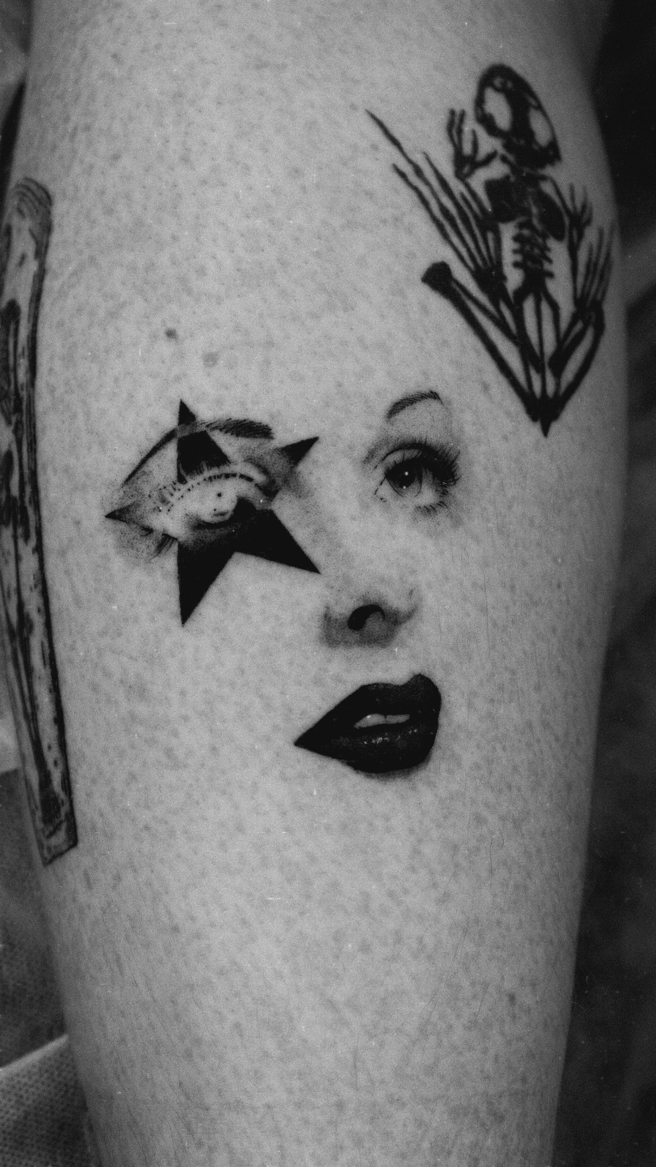 Black and grey tattoo combining a woman's eyes and lips with a star and skeletal hand.