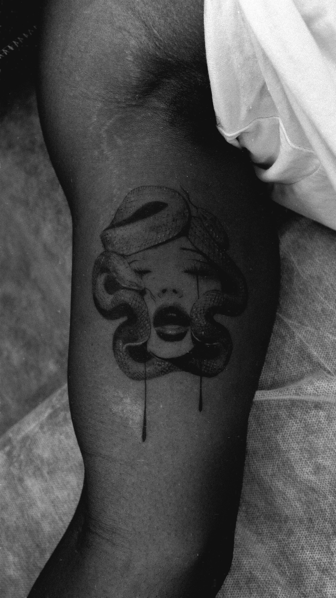 Black and grey arm tattoo of a surreal face with curved shapes around the head.