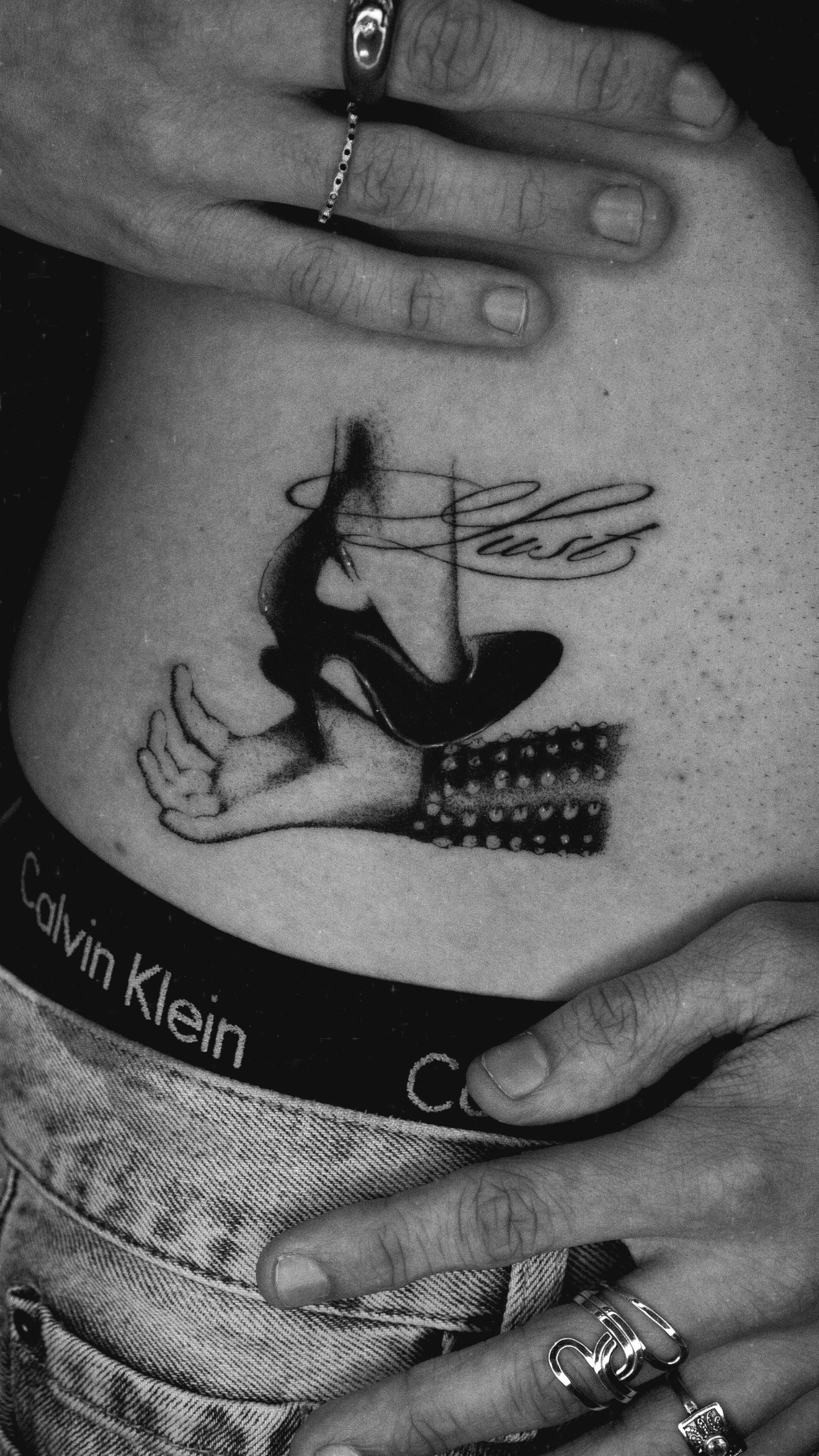 Black and grey torso tattoo of a stylized hand with an elongated finger and flowing linework.